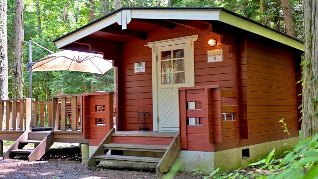a small red cabin with a porch and an umbrella at Work Shop Camp Resort Forest and Lake Paradise - Vacation STAY 85274v in Fujikawaguchiko