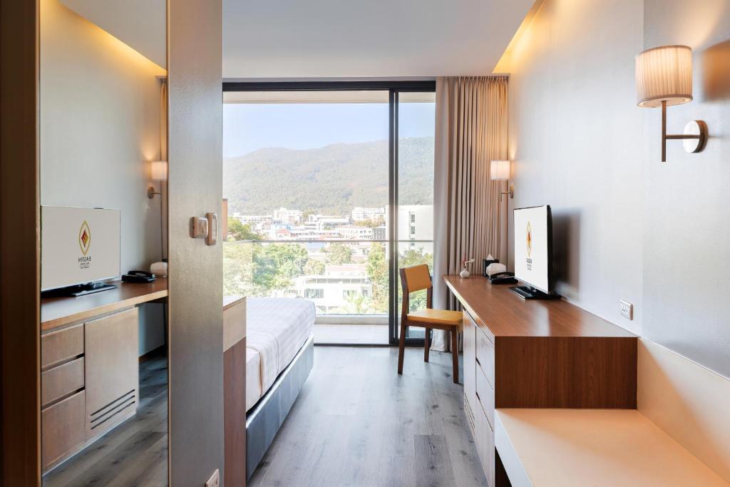 A narrow modern room with a bed, two work surfaces and a mountain-facing glass door.