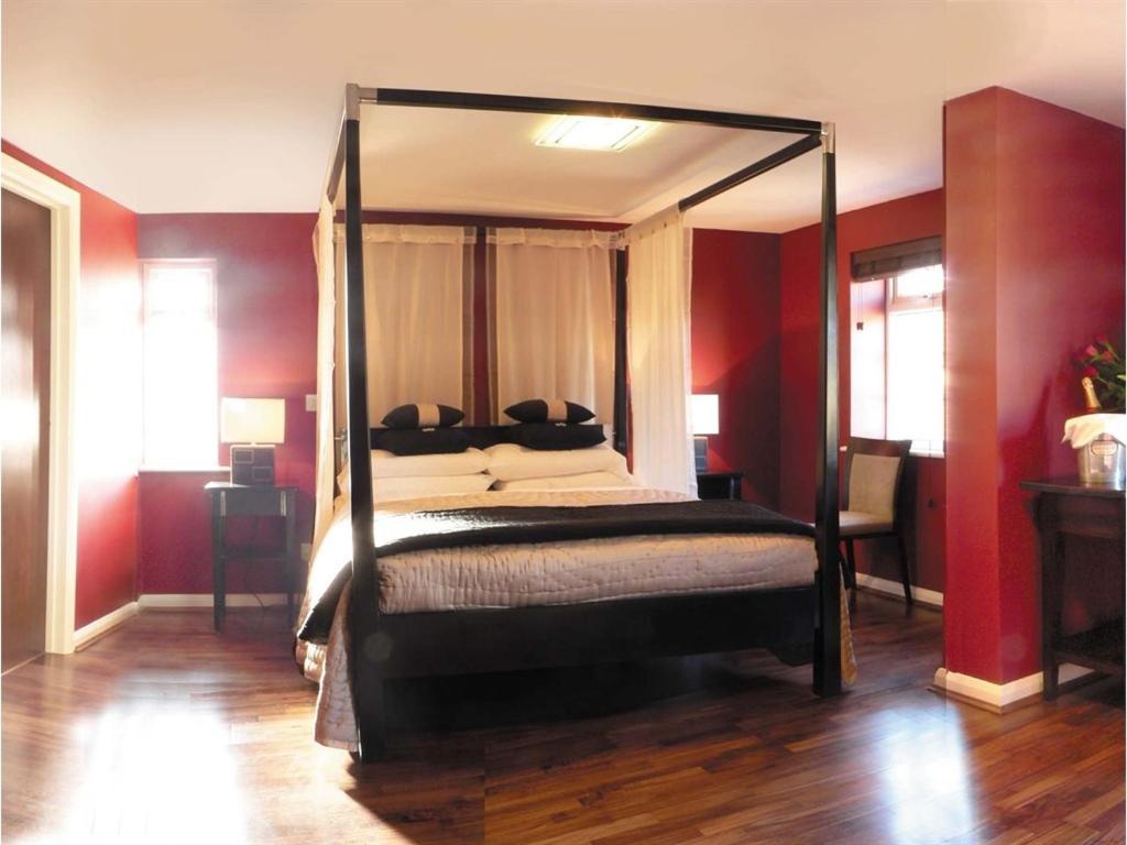 a bedroom with a canopy bed with red walls at Nap Inn Savoro in Barnet