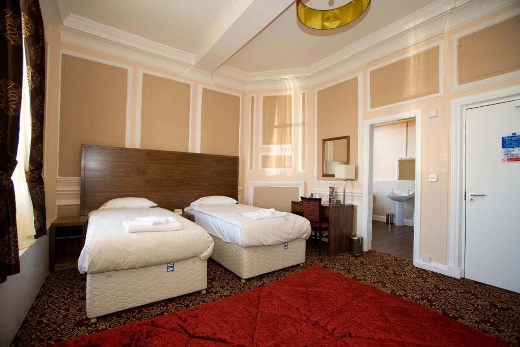 two beds in a room with a red rug at The Three Tuns Hotel Wetherspoon in Thirsk