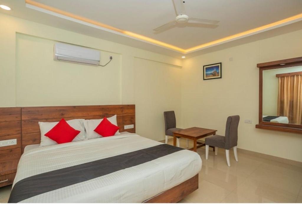 a bedroom with a bed with red pillows and a table at HOTEL SAVI iNN in Bangalore
