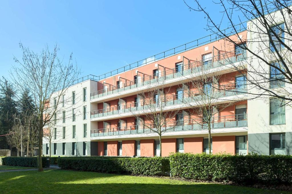 un grand immeuble avec des buissons en face dans l'établissement Zenitude Hôtel-Résidences - Versailles Saint-Cyr-l'Ecole, à Saint-Cyr-lʼÉcole