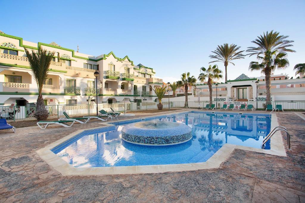 a swimming pool in front of a building with palm trees at Casa David Prieto 2 Habitaciones in Caleta De Fuste