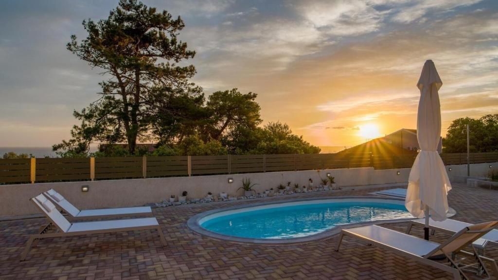 uma piscina com um guarda-sol e cadeiras e um visor de sol em Arktos Sunset Villa em Cefalônia