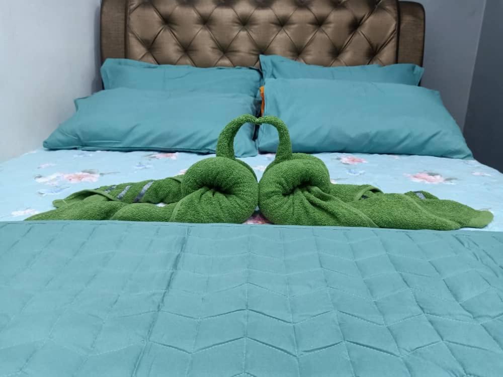 a green stuffed animal laying on a bed at Kayangan Apartment in Kangar