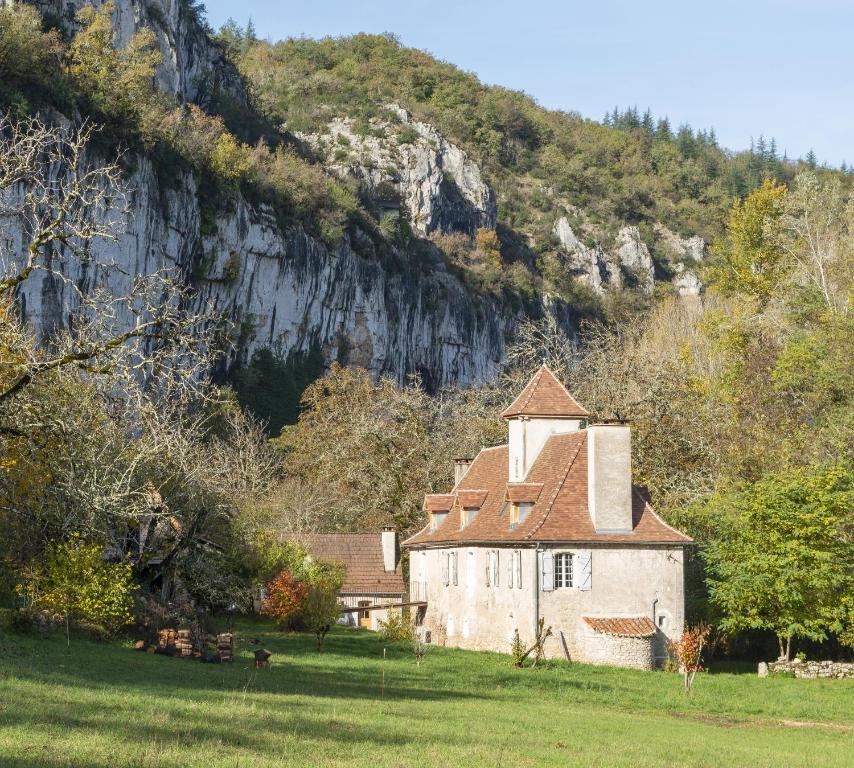 an old house in a field next to a mountain at La maison de Ganil in Saint-Cirq-Lapopie