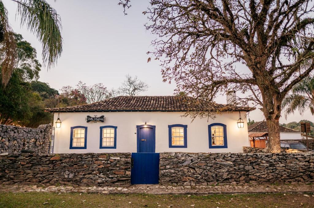 a white house with a stone wall and a tree at Pousada Boutique Villa Chafariz Tiradentes in Tiradentes