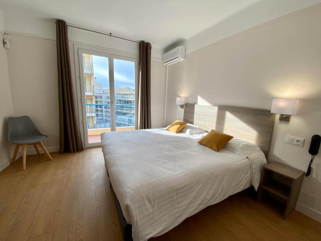 a bedroom with a large bed and a large window at Hotel Courbet in Juan-les-Pins