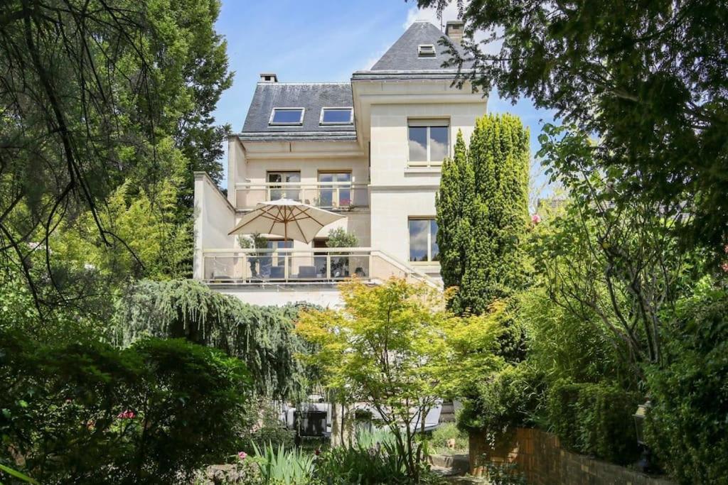 une grande maison blanche avec un parasol dans un jardin dans l'établissement Villa des Oliviers, à Fontenay-sous-Bois