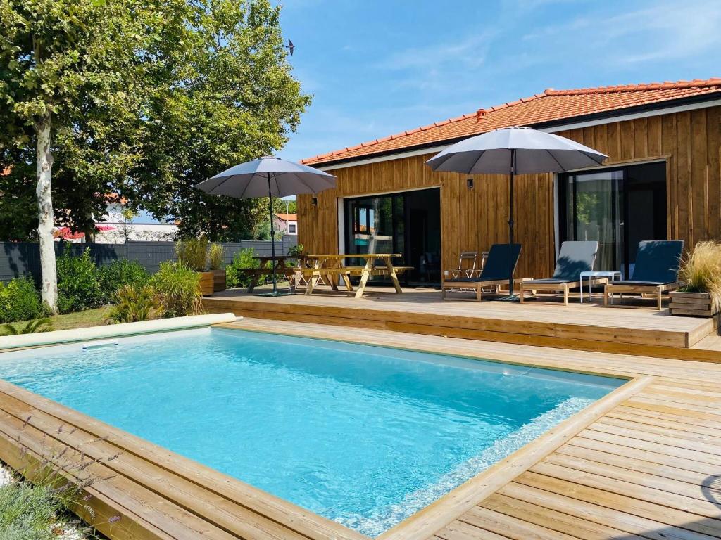 a pool with a deck and a house with umbrellas at CABANE DE BRICE à ARES in Arès