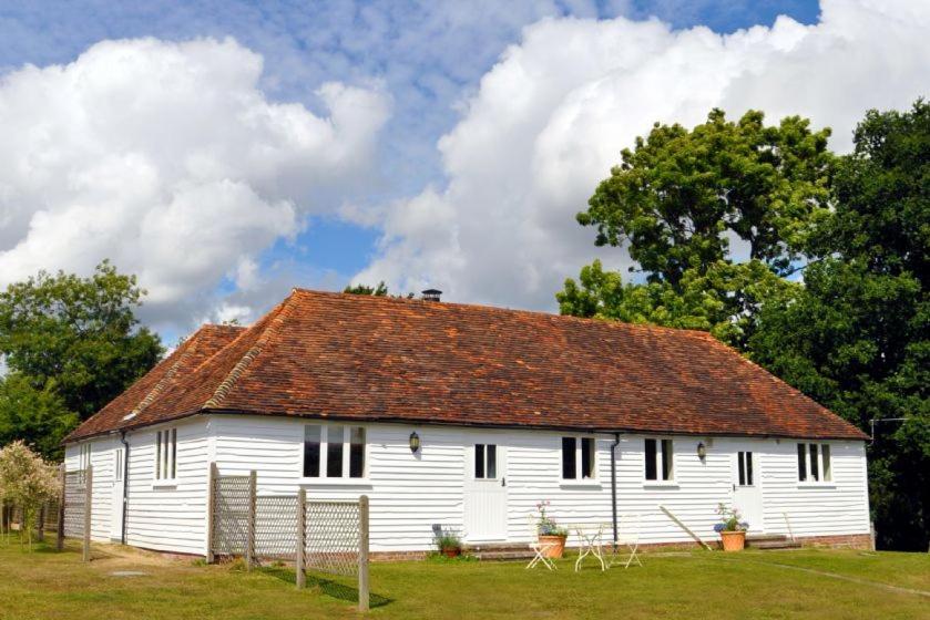 a white barn with a red roof on a field at Coach House Barn in Cranleigh