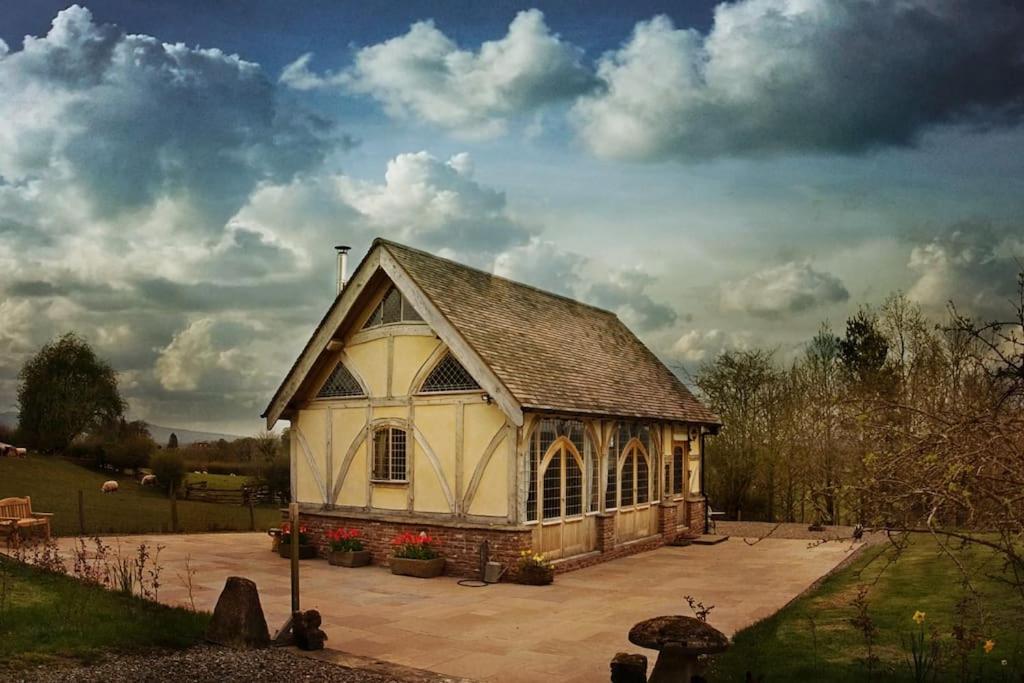 a large white building in a field with a cloudy sky at Ebony Cottage in Tenbury