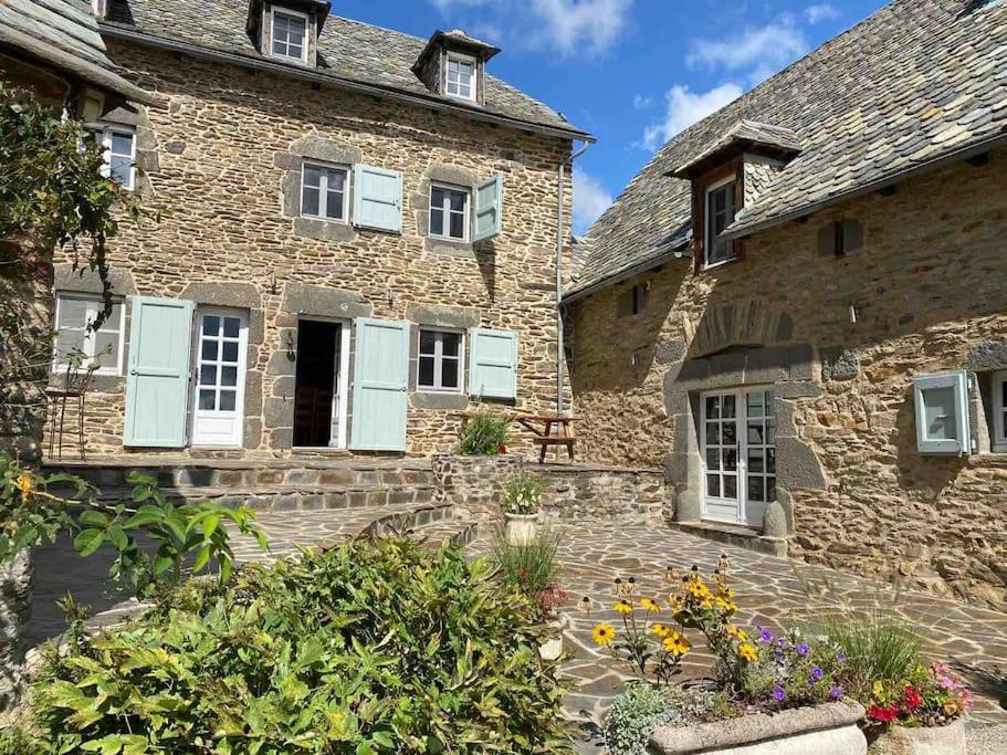 an old stone building with blue shuttered windows and flowers at La Roulière en Aubrac in Montpeyroux