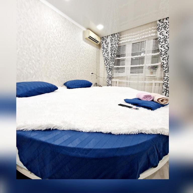 Una cama con sábanas azules y blancas y una ventana en 1 ком Квартира в центре en Uralsk
