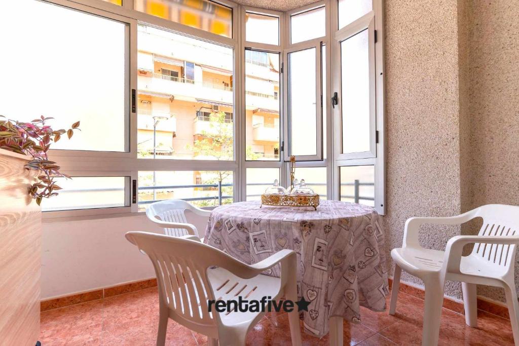 Zimmer mit einem Tisch, weißen Stühlen und Fenstern in der Unterkunft rentafive Nuevo Junto a la Playa Ascensor in Santa Pola
