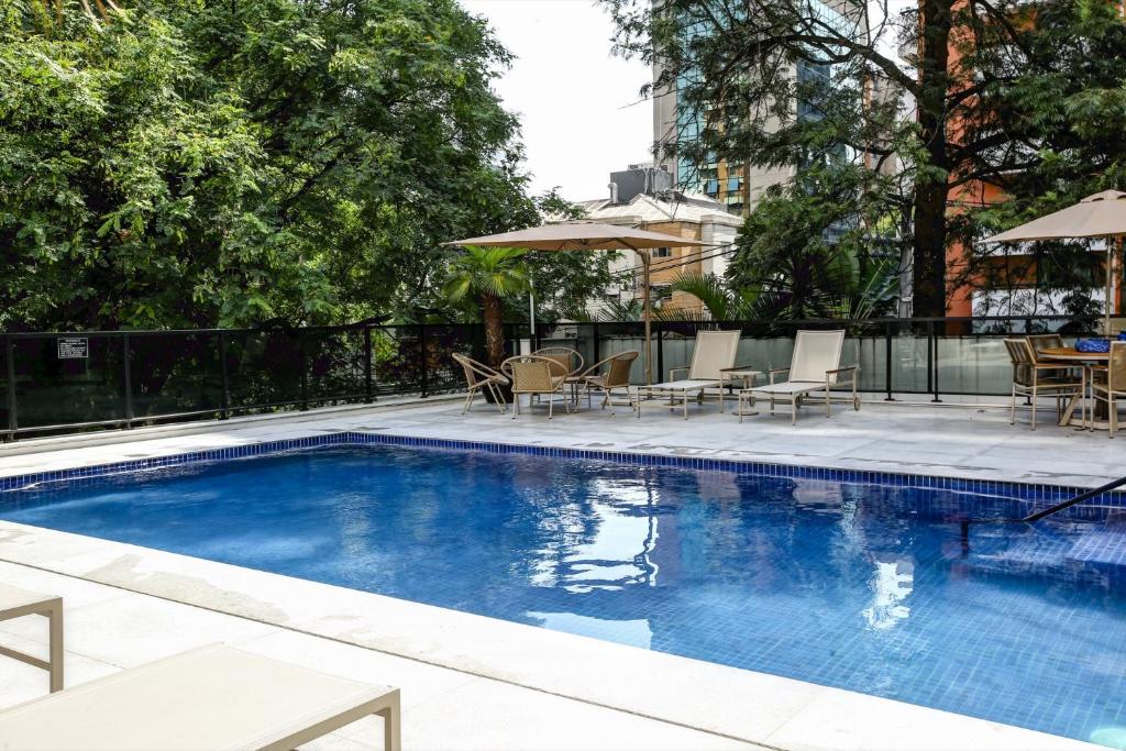 a swimming pool with chairs and a table and umbrella at Roomo Transamerica SP Itaim Bibi in Sao Paulo