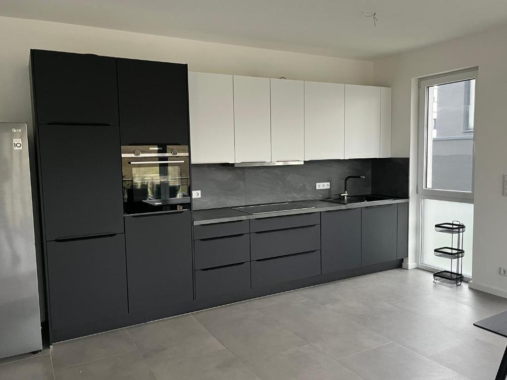 eine Küche mit weißen Schränken und einem schwarzen Kühlschrank in der Unterkunft Luxus Neubauwohnung mit Blick auf den Phönix-See in Dortmund