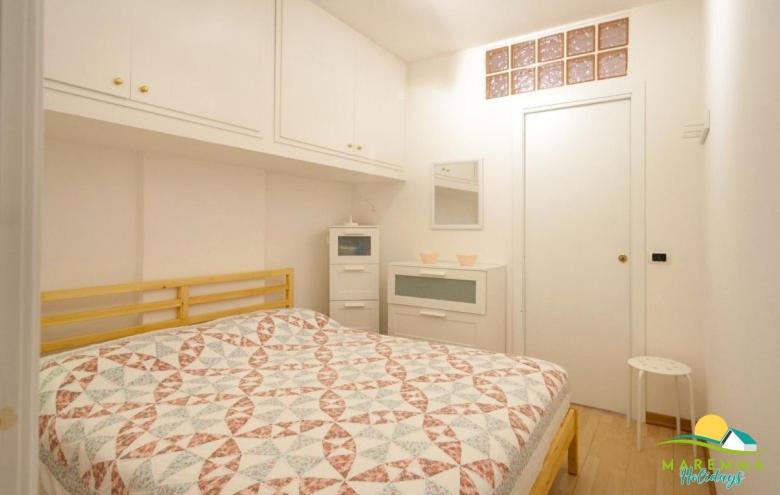 ein weißes Schlafzimmer mit einem Bett und einer Küche in der Unterkunft Maremma Holidays:Pini Apartment in Follonica