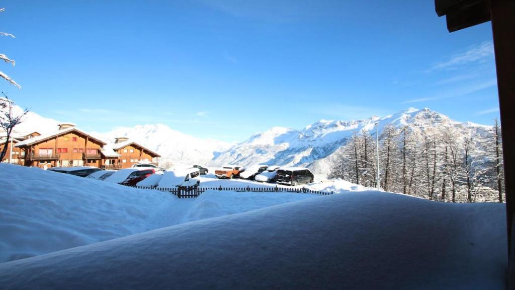 a snow covered yard with cars parked in front of a mountain at Résidence Dame Blanche - Chalets pour 6 Personnes 721 in Narreyroux