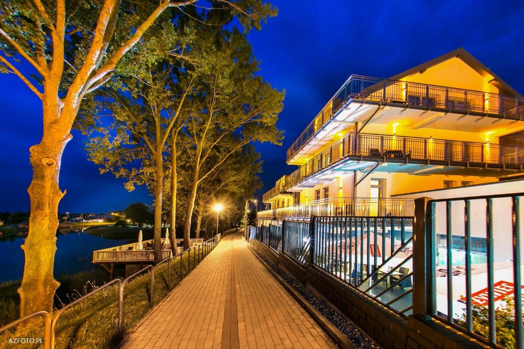 a building on a walkway next to a river at night at Pensjonat & Spa Raj in Rajgród