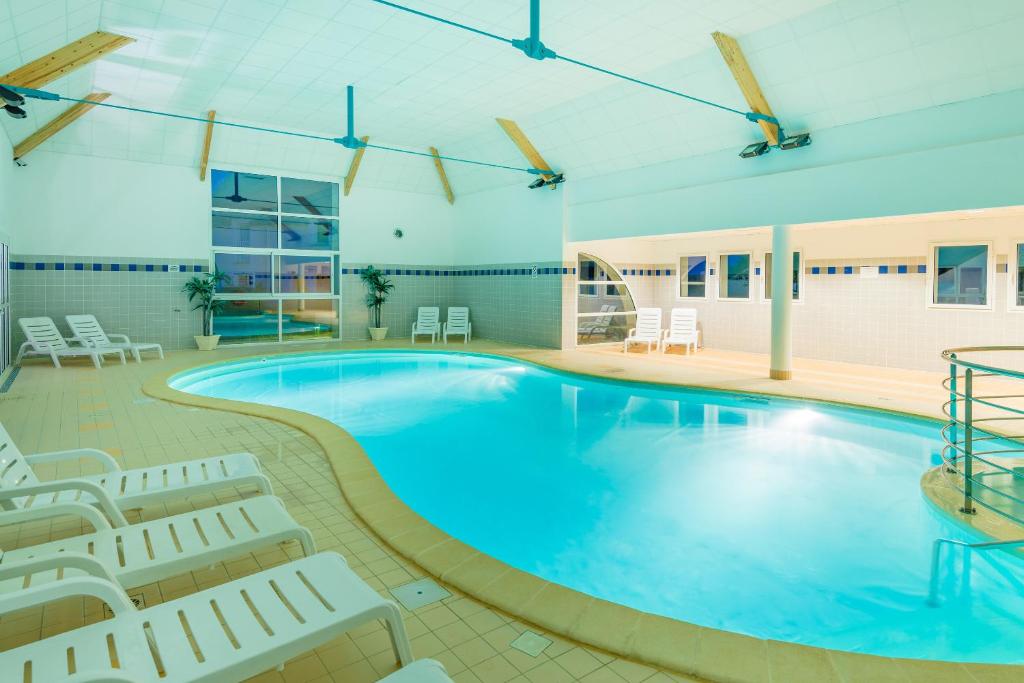 - une grande piscine avec des chaises et des chaises dans un bâtiment dans l'établissement Lagrange Vacances Les Jardins Renaissance, à Azay-le-Rideau