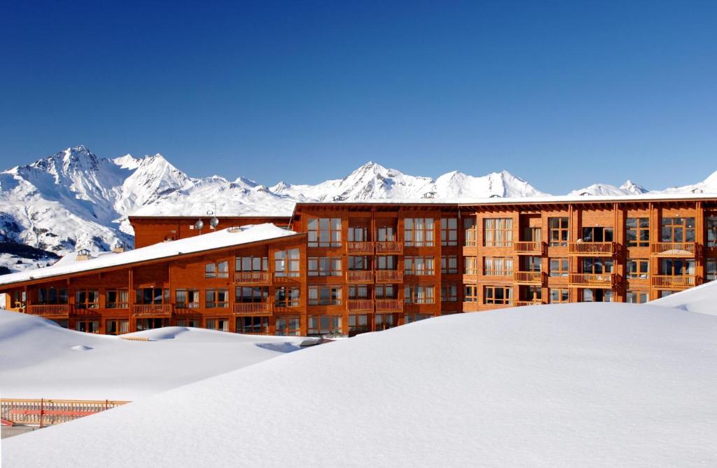 a building in the snow with mountains in the background at Résidence Prestige Odalys Edenarc in Arc 1800