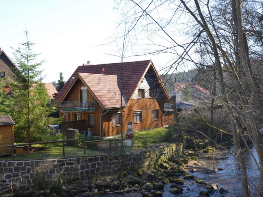 ein Holzhaus mit einer Steinmauer neben einem Fluss in der Unterkunft Holiday home Hexenstieg in the Harz Mountains in Elend