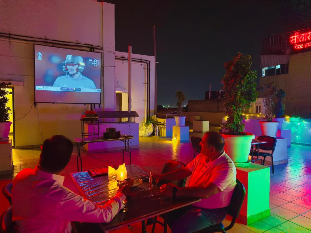 Due uomini seduti a un tavolo di fronte a una TV di Shree Narayana Hotel-BAR-Rooftop Terrace-Disc a Udaipur