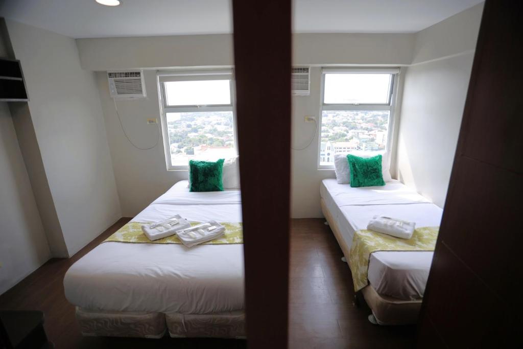 twee bedden in een kamer met twee ramen bij Homes by Gilmore Tower Suites in Manilla