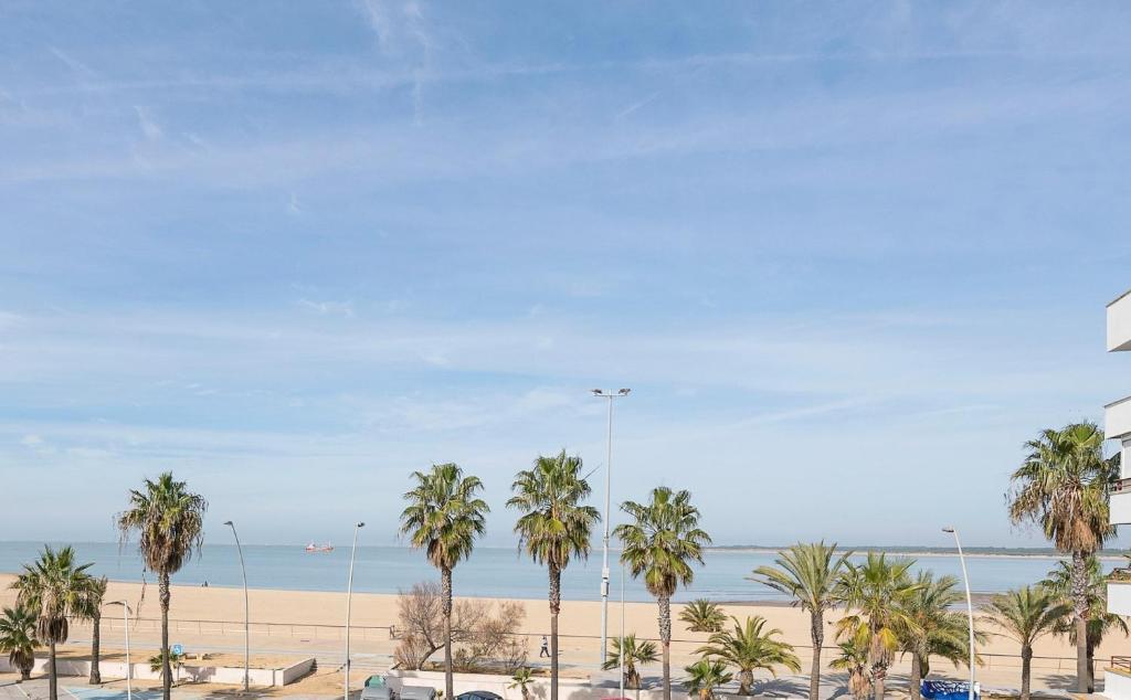 een uitzicht op een strand met palmbomen en de oceaan bij Ventana a Doñana in Sanlúcar de Barrameda