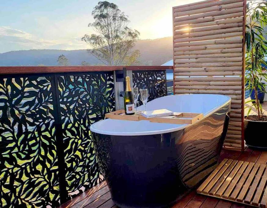 a bath tub on a deck with a bottle of wine at Mountview Alpaca Farmhouse in Canungra