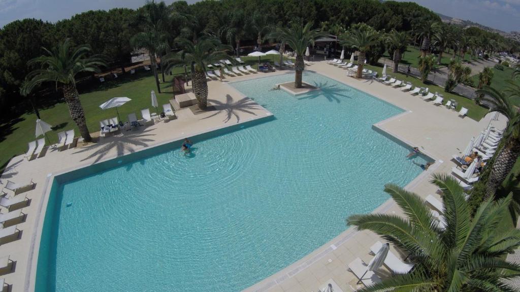 an overhead view of a large swimming pool with chairs and palm trees at Eureka Palace Hotel Spa Resort in Cassibile