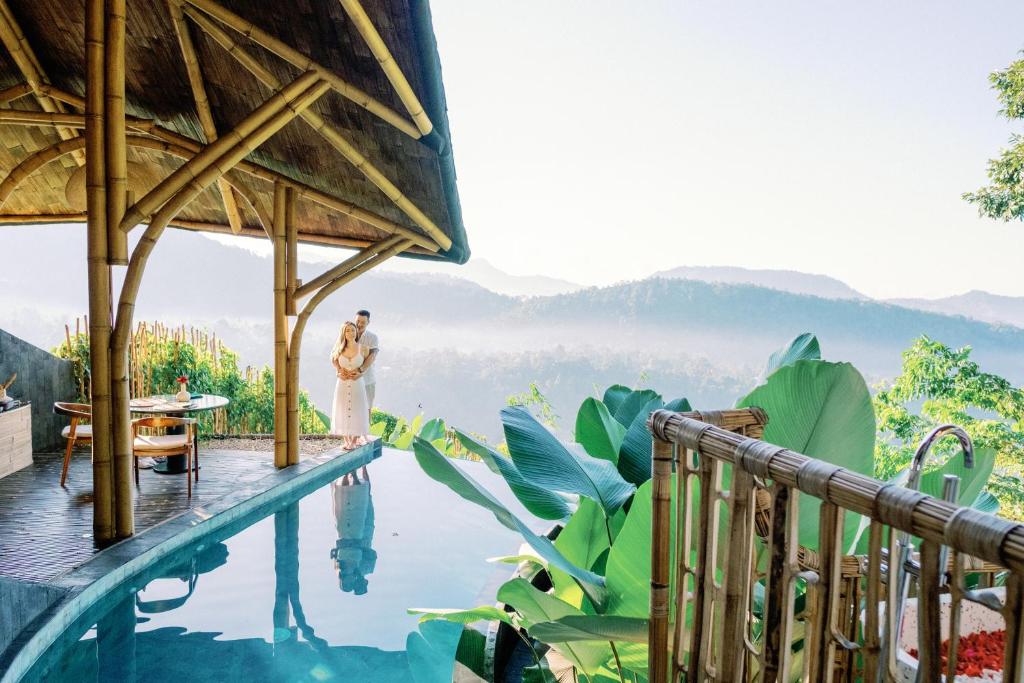 een vrouw naast een zwembad in een resort bij Dreamy Cliffside Bamboo Villa with Pool and View in Klungkung