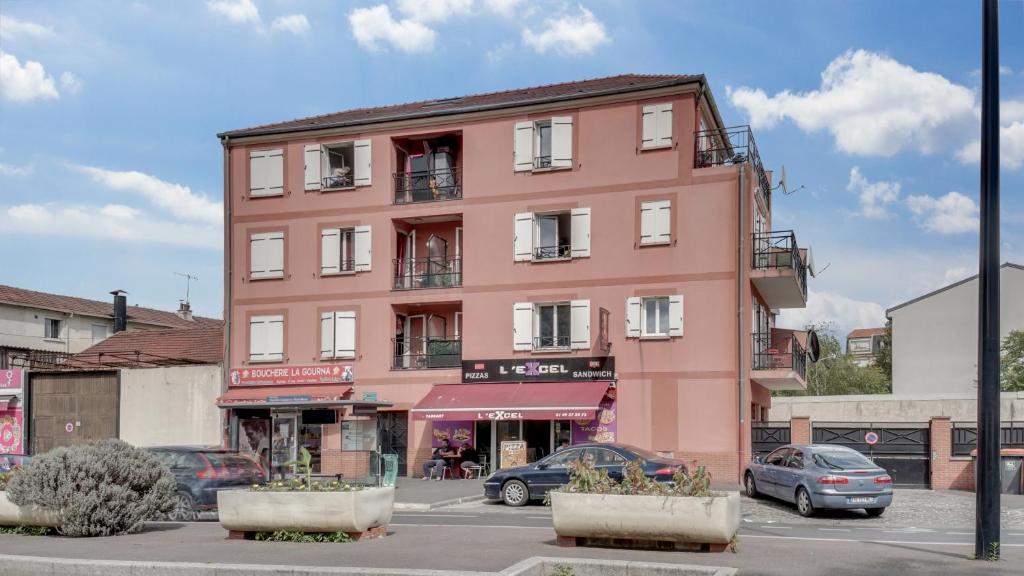 a pink building with cars parked in a parking lot at Chic apart with parking and balcony near Paris in Aubervilliers