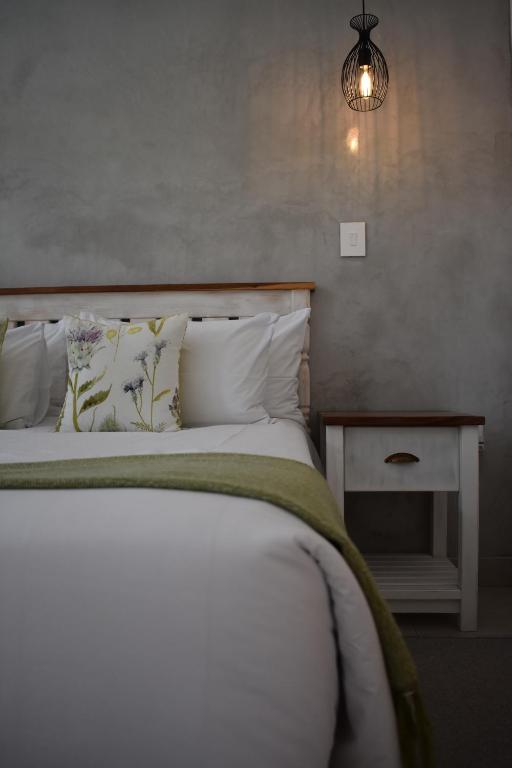 Symponia Guesthouse في Ghanzi: غرفة نوم بسرير ومخدات بيضاء ومصباح