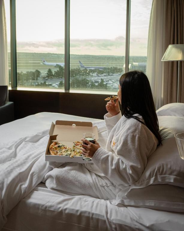 a woman sitting in bed eating a box of pizza at FLY INN BAKU in Baku