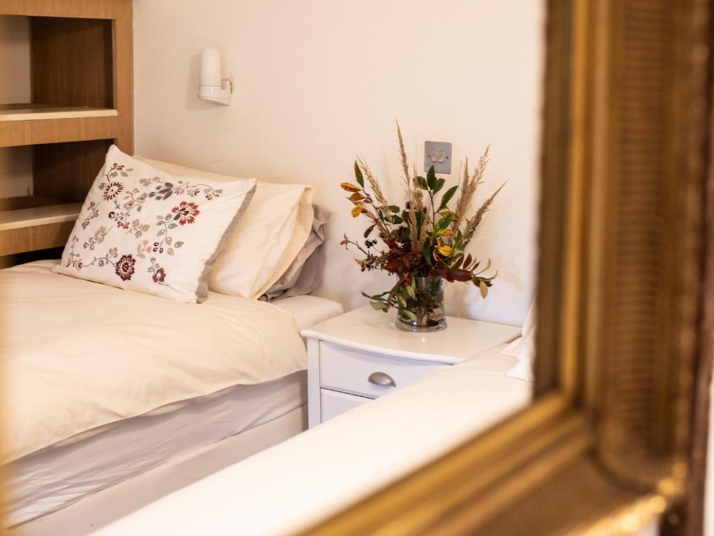 a small bedroom with a bed and a vase of flowers at Betty's Cottage in Burford
