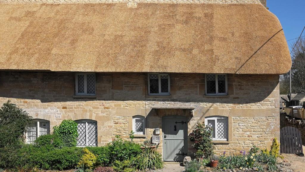 an old stone house with a thatched roof at Betty's Cottage in Burford