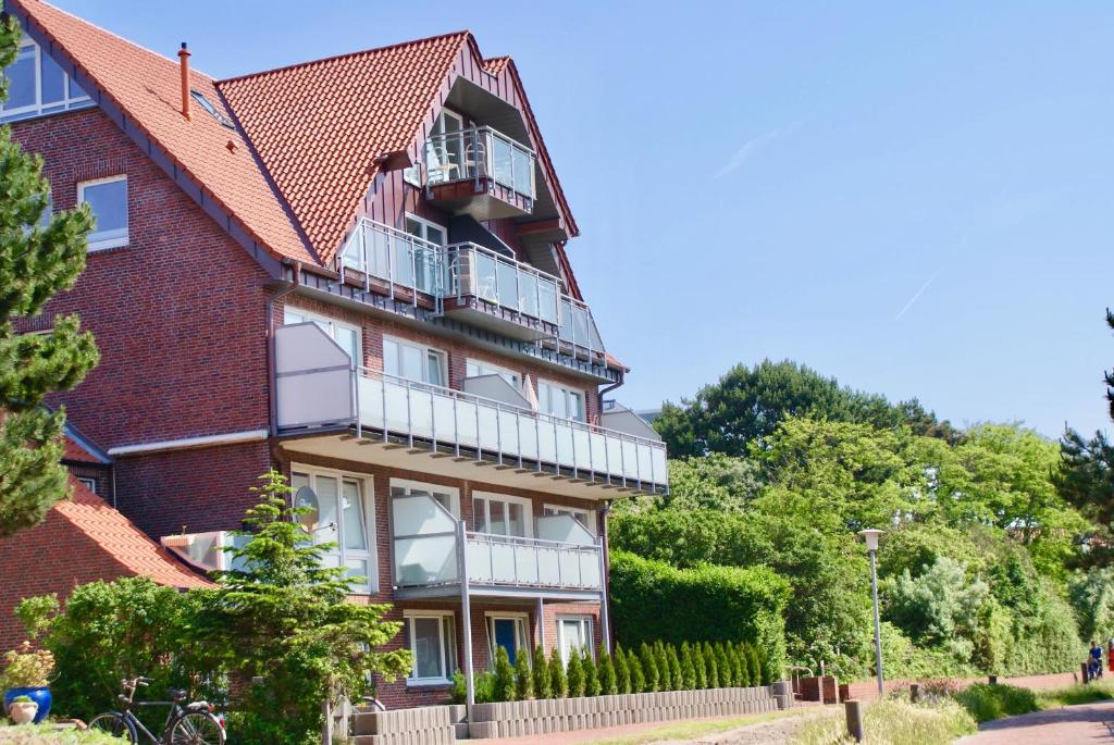 - un bâtiment en briques rouges avec un balcon et des arbres dans l'établissement Strandhaus Rose, à Juist