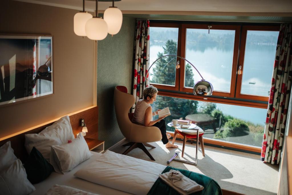 una mujer sentada en una silla en una habitación con ventana en Apartments am See en Egg am Faaker See