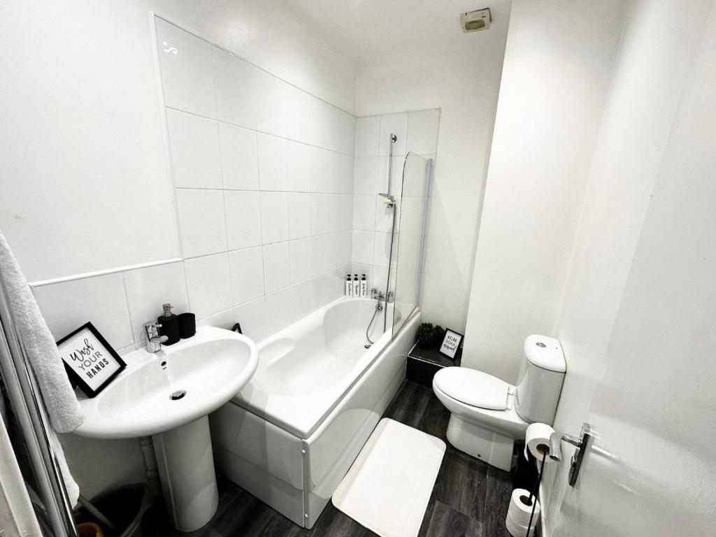 La salle de bains blanche est pourvue d'un lavabo, d'une baignoire et de toilettes. dans l'établissement Leicester City Centre Apartment with Parking, à Leicester