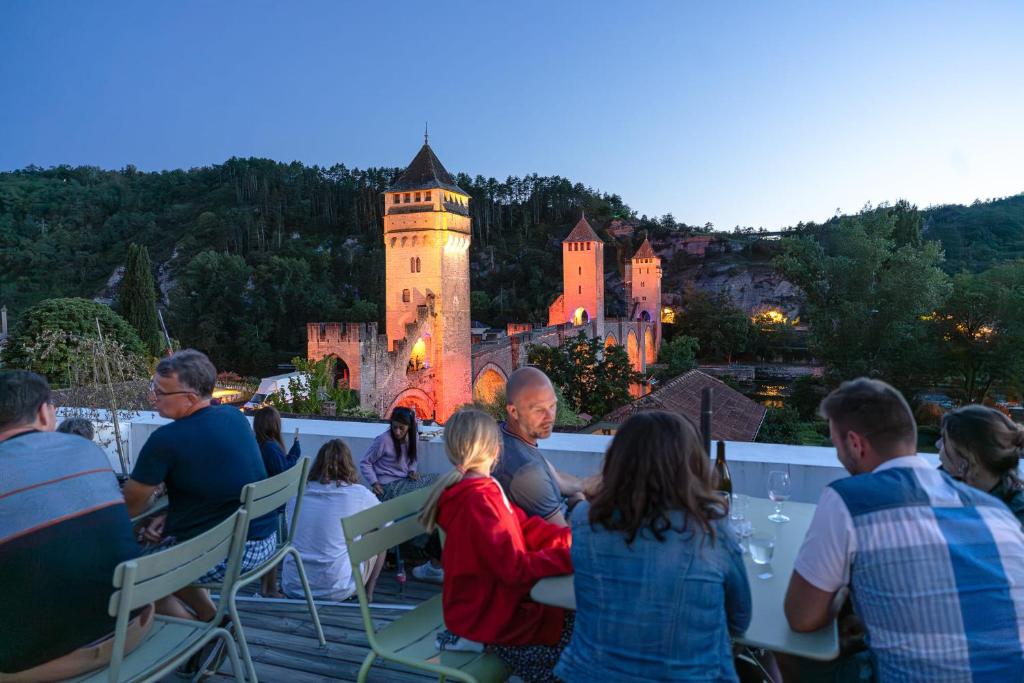 Auberge de Jeunesse HI Cahors في كاهور: مجموعة من الناس جالسين على سقف يطل على قلعة