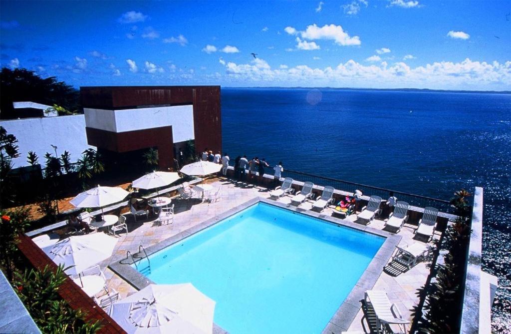 uma piscina com cadeiras e guarda-sóis junto ao oceano em Sol Victoria Marina Flat em Salvador