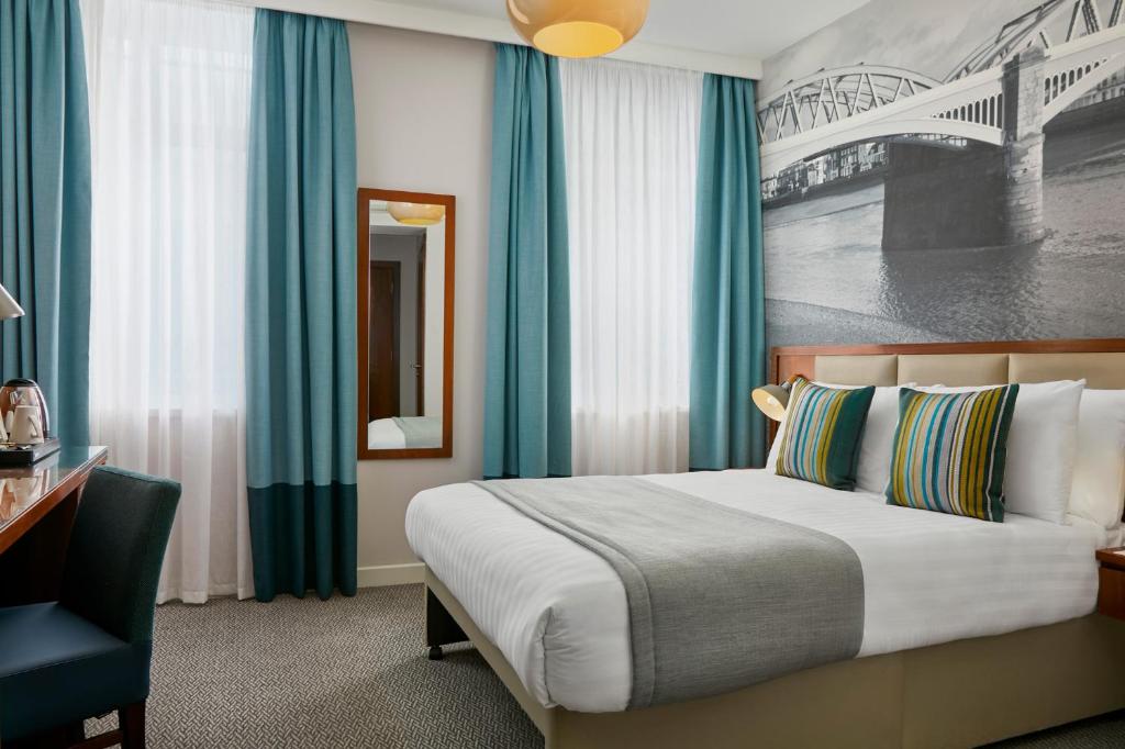 a bedroom with a bed with blue curtains and a desk at Seraphine Hammersmith Hotel in London