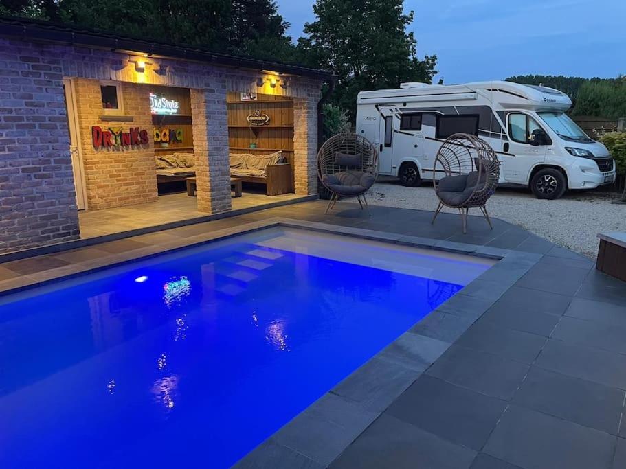 a swimming pool in front of a rv and a parked van at Camper met sauna en zwembad in de rand van de Vlaamse Ardennen in Haaltert