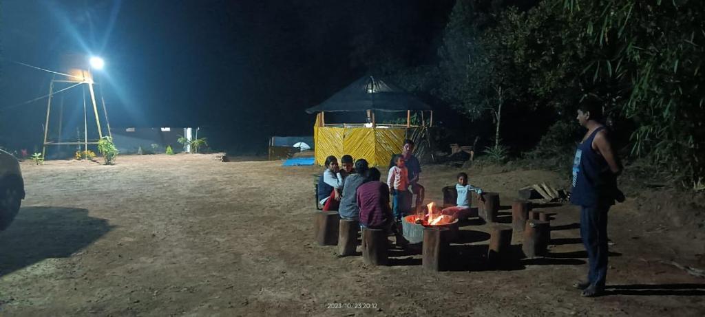 un grupo de personas sentadas alrededor de una mesa por la noche en Coorg Derala Camping Tent House en Madikeri