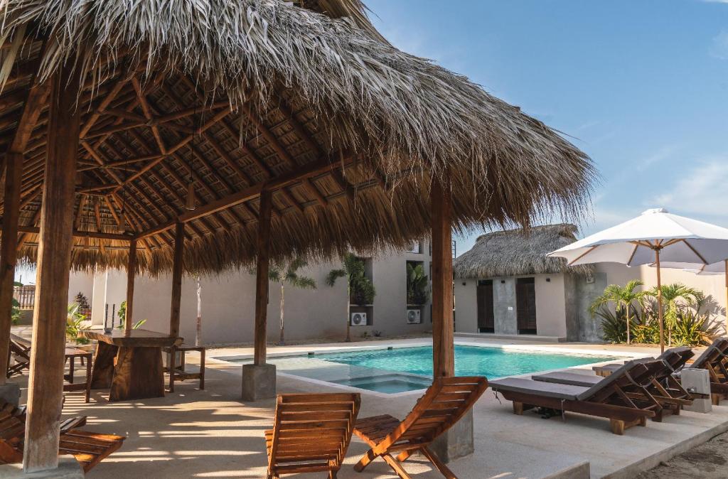 a resort with a swimming pool with chairs and a straw umbrella at La Barra Resorts Puerto Escondido in Puerto Escondido