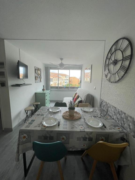 Cette chambre comprend une table avec des chaises et une horloge murale. dans l'établissement Petit Cocon a deux pas de la mer, à Saint-Cyprien