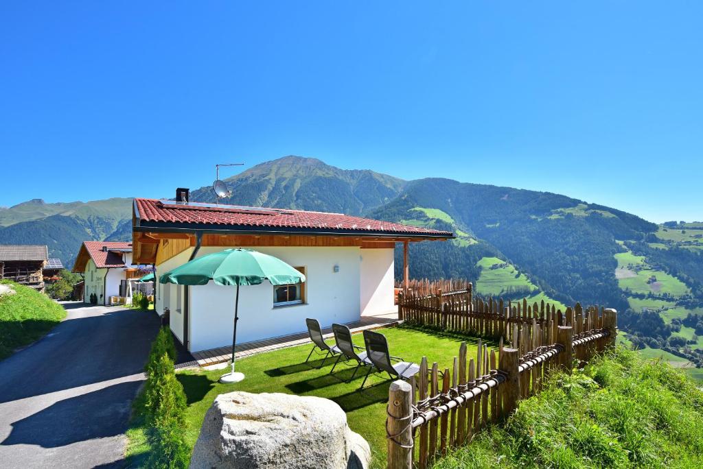 una casa con una sombrilla verde, sillas y una valla en Tratterhof Apt Astjoch, en Vandoies