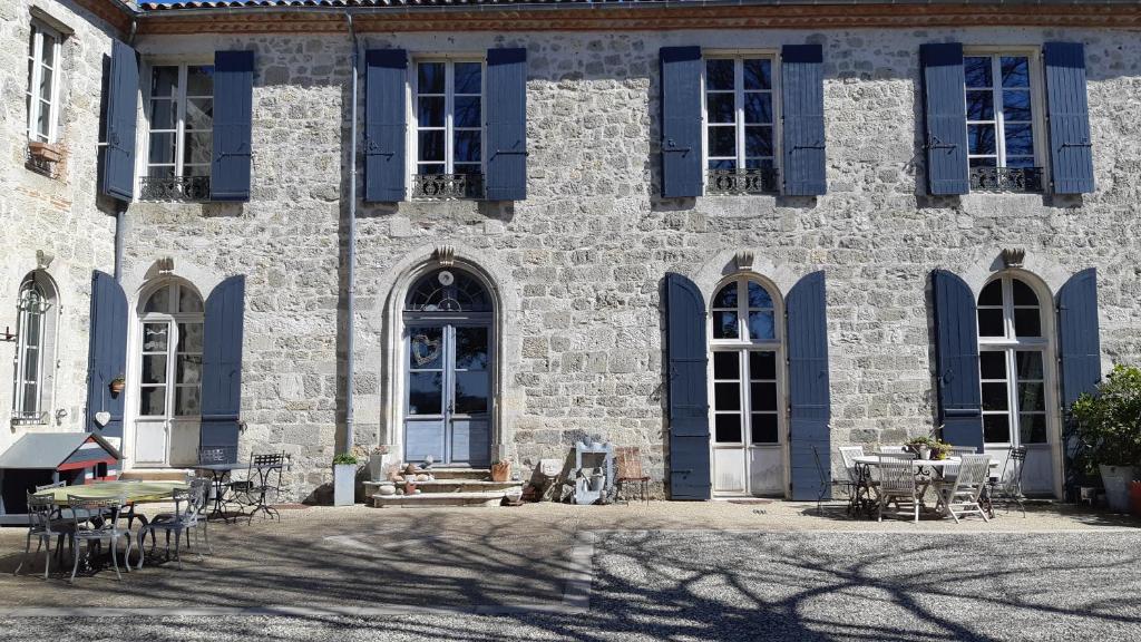 un gran edificio de piedra con persianas y mesas azules en Au Bonheur d'Alphonse en Lusignan-Petit